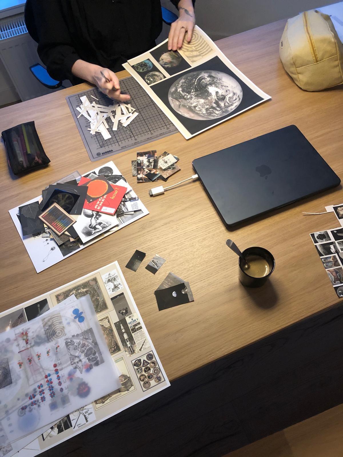 Work in progress: cut-out prints, transparent sheets and a printed photograph of the Earth on a desk