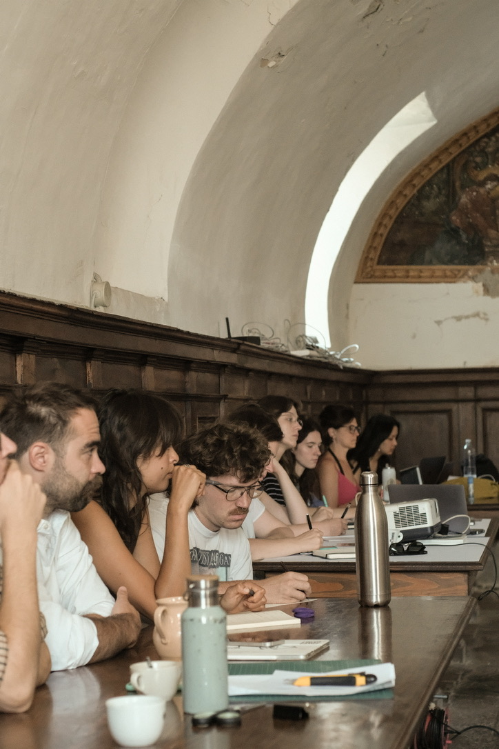 Participants listening and taking notes at long wooden tables under a vaulted ceiling
